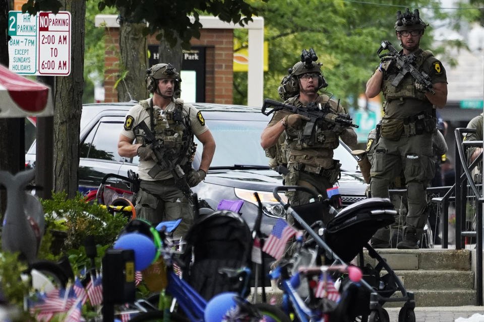 Armed law enforcement officers survey an area of town in Highland Park, Ill.