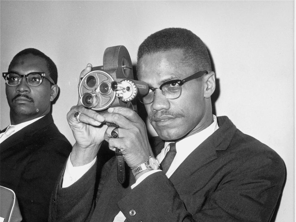 Malcolm X, black nationalist leader, is shown with his 16mm Bell and Howell motion picture camera at JFK International airport, July 9, 1964, prior to his departure for Egypt and Africa and the African Nations Conference.