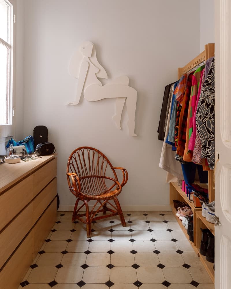 Walk-in closet with hanging clothes, wicker chair, sculpture, and wooden dressers.