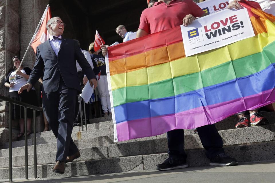 A man in a dark suit walks down steps near a person holding a rainbow banner that says Love Wins