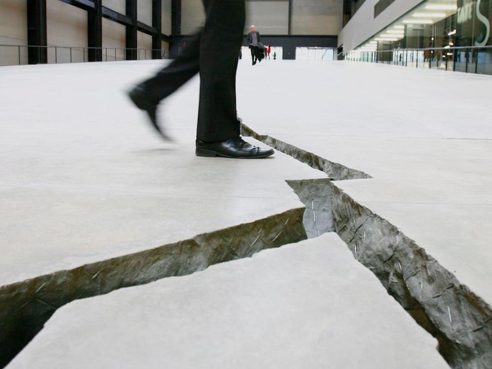 A man poses for the camera as he walks over Doris Salcedo's work, Shibboleth - a giant crack in the floor of the Tate Modern in London October 8, 2007. Colombian artist Doris Salcedo has filled Tate Modern's cavernous Turbine Hall with a hole as the latest work in the art gallery's annual installation series. Dubbed Shibboleth after the biblical massacre of the same name, the work is a trench dug into the concrete floor of the former power station and running its entire 167 metres length starting as a crack and ending as a chasm.  (BRITAIN)