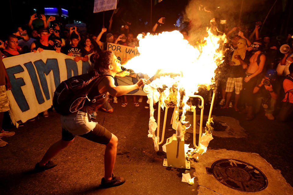 A girl spits fire on a bus turnstile set on a street in protest against the increase on bus fares in Rio de Janeiro, Brazil, Monday, Feb. 10, 2014. Anti-government protests erupted across Brazil last June, hitting their peak as 1 million Brazilians took to streets on a single night, calling for better schools and health care and questioning the billions spent to host this year's World Cup and the 2016 Olympics. The protests have since diminished in size, but remain violent. (AP Photo/Leo Correa)