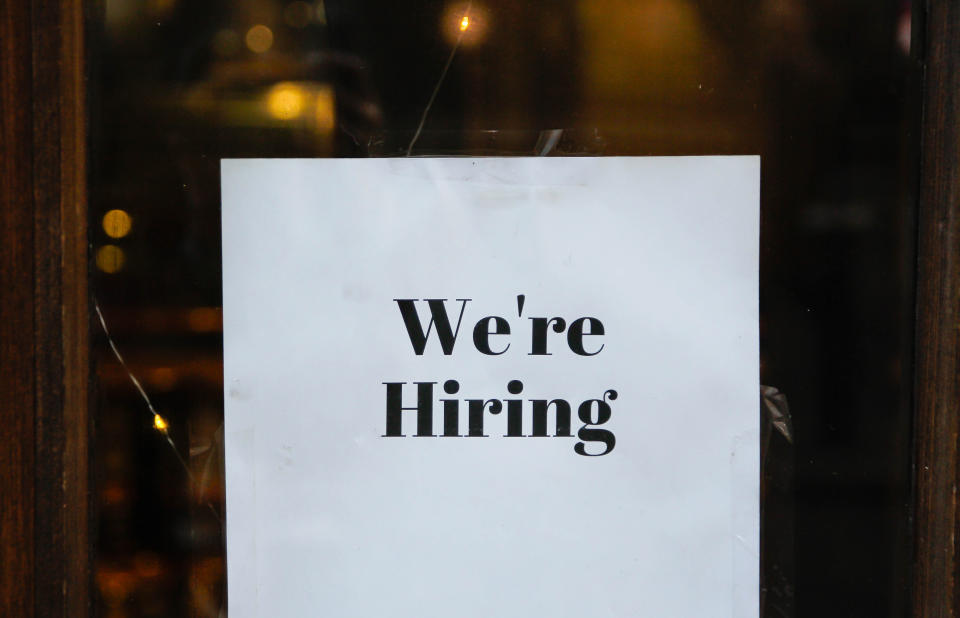 A white sign on a glass door reads "We're Hiring" in bold black letters