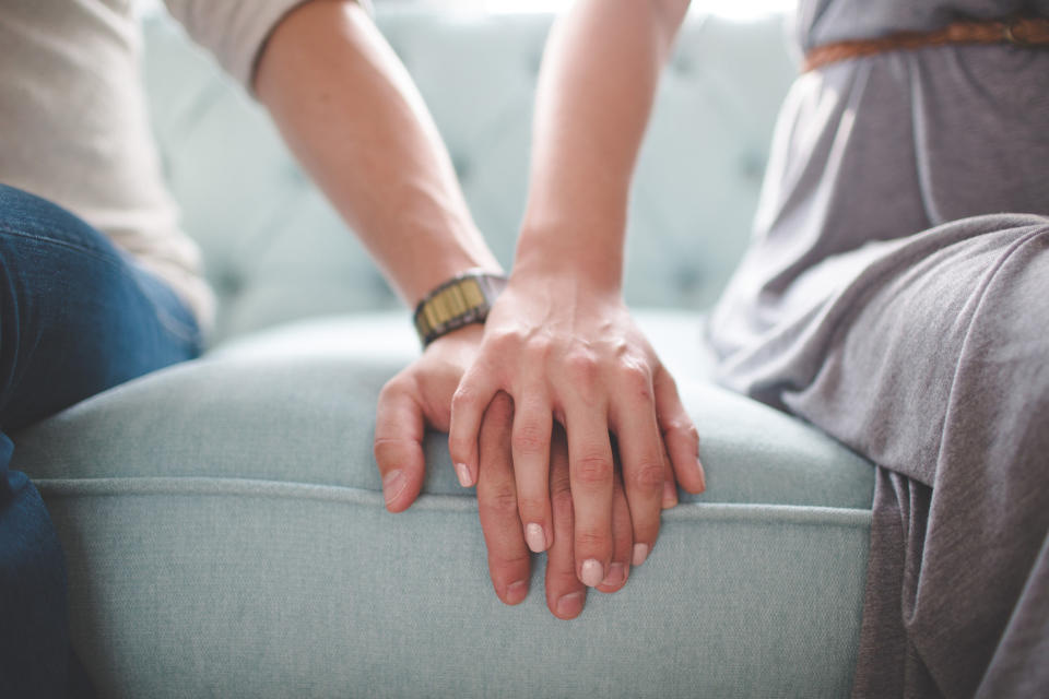 The hands of two people sitting on a couch touching