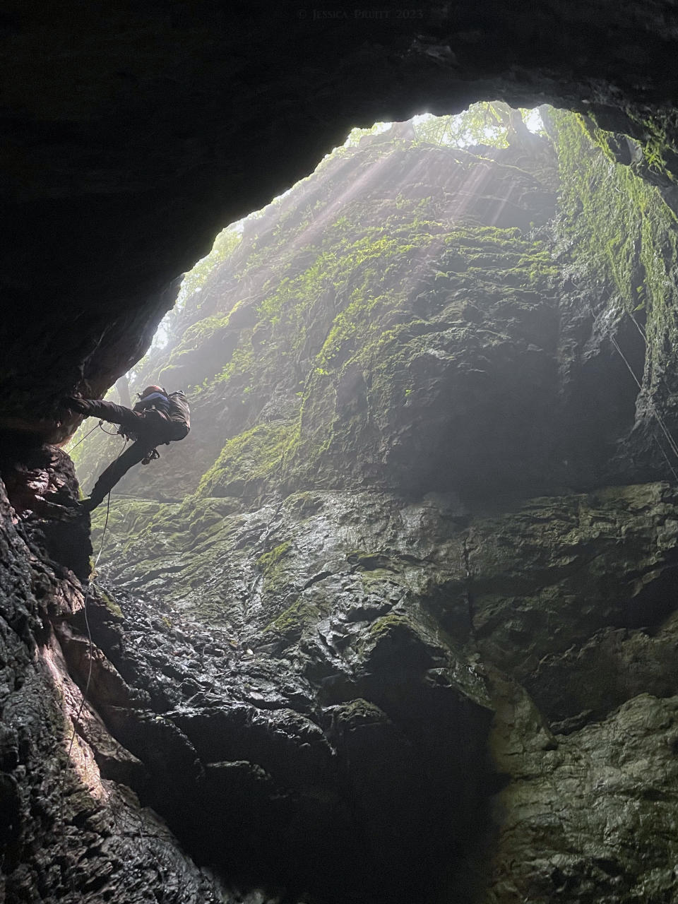 A caver descending into a cave from a brightly lit entrance