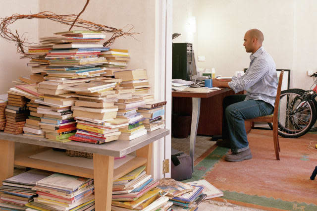 Man working in home office by bikes and books piled by doorway, mess,  messy, clutter, houseCasual Clothing, Horizontal, Full L