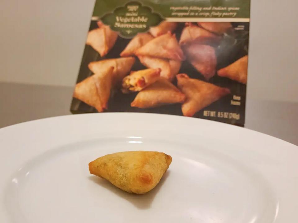 A samosa with browned edges on a white plate with a green box