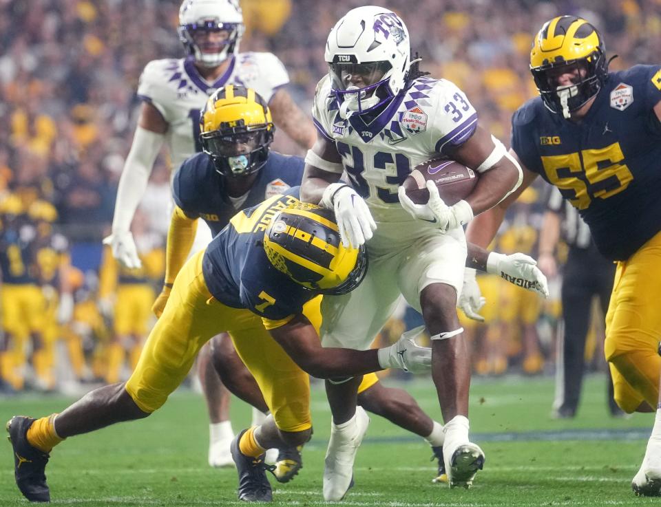 TCU running back Kendre Miller (33) tries to break away from Michigan Makari Paige (7) past during the 2022 Fiesta Bowl at State Farm Stadium.