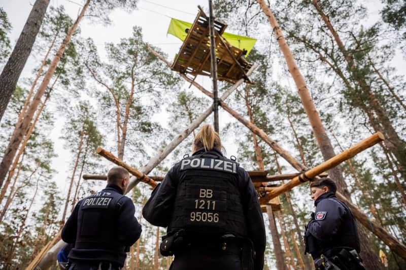 Police officers stand at the camp of the "Stop Tesla" initiative, erected in a pine forest near the Tesla Gigafactory Berlin-Brandenburg. The permit for the camp expired on Friday at midnight and is expected to be evacuated next weekend. Sebastian Gollnow/dpa