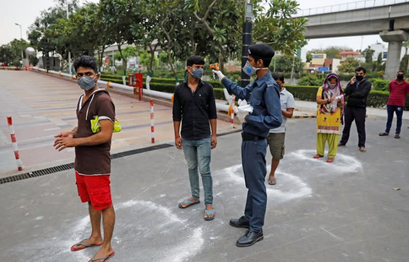 A private security guard uses an infrared thermometer to measure the temperature of people waiting to enter a supermarket during the coronavirus disease (COVID-19) outbreak in New Delhi