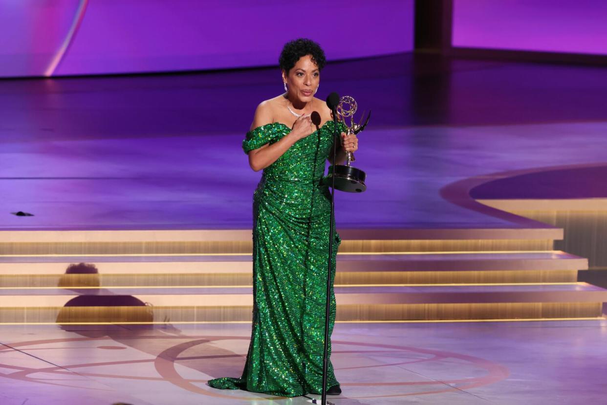 Liza Colón-Zayas in a green dress onstage holding an Emmy