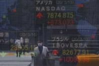 A woman wearing a protective face mask, following an outbreak of the coronavirus disease (COVID-19), is reflected in a screen displaying NASDAQ movements outside a brokerage in Tokyo