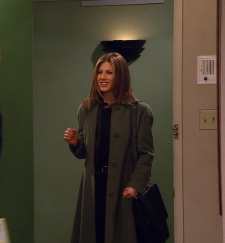 Rachel wearing pants, a shirt, a blazer, a large coat, and she has a briefcase