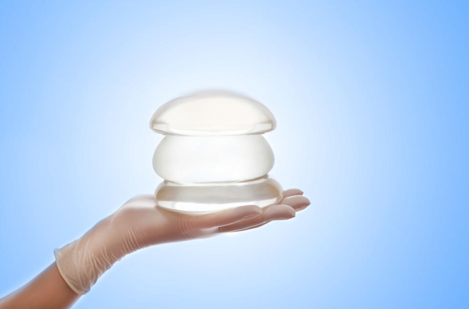 A medical professional wearing gloves holds a stack of silicone breast implants in their hand