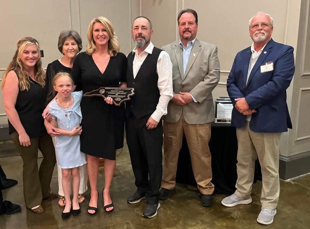 (From left) Gaston County Clerk to the Board Donna Buff's daughter Taylor, granddaughter Olivia, mother Becky, husband Robby, and Gaston County Commissioners Allen Fraley and Bob Hovis surround her as she poses with her award.
