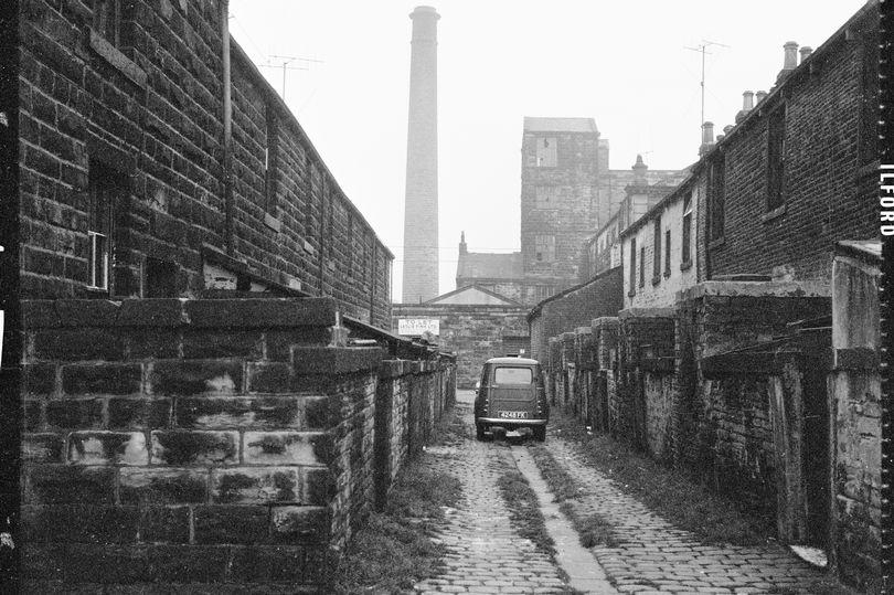 Richard Street, Burnley, Lancashire, circa 1966 - circa 1974. A car parked in the cobbled ginnel (alley) running between Milton Street and Tentre Street viewed from Richard Street with Pentridge Mill and mill chimney partially visible in the background. The terraces shown here were demolished in the late 1960s. Holly House flats now occupies the site. Artist Eileen Deste