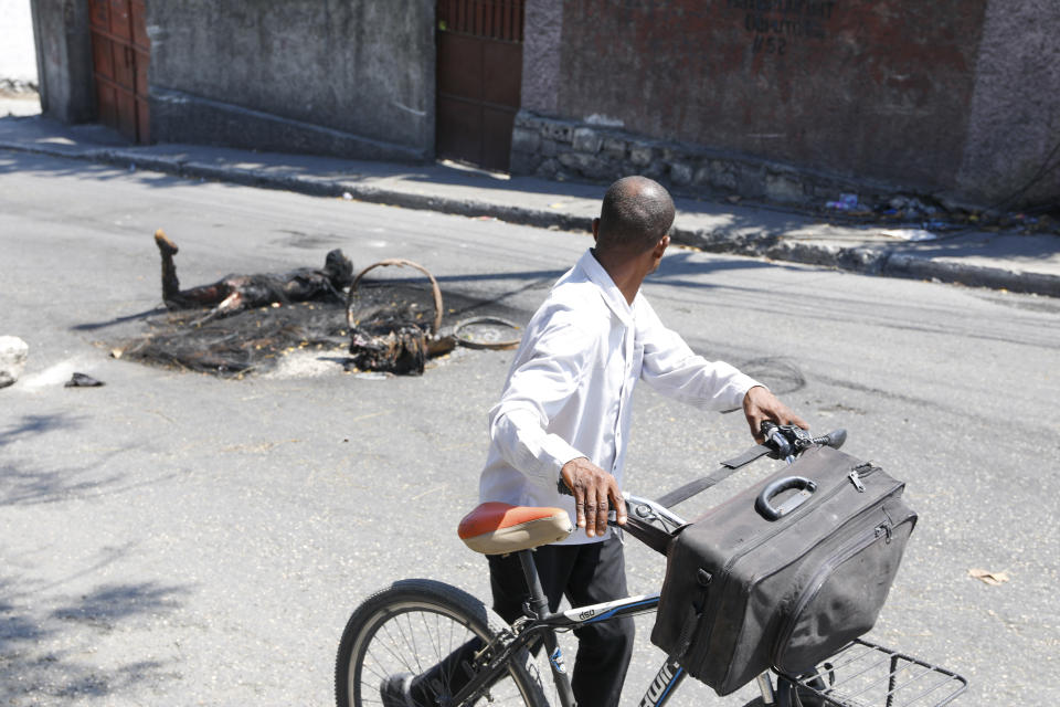 A man pushes his bike past the body of a person who was killed and set on fire in Port-au-Prince, Haiti, Tuesday, March 5, 2024. Prime Minister Ariel Henry has been absent since the country's latest and most serious outbreak of violence started the previous week, and armed groups have seized on the power void. (AP Photo/Odelyn Joseph)