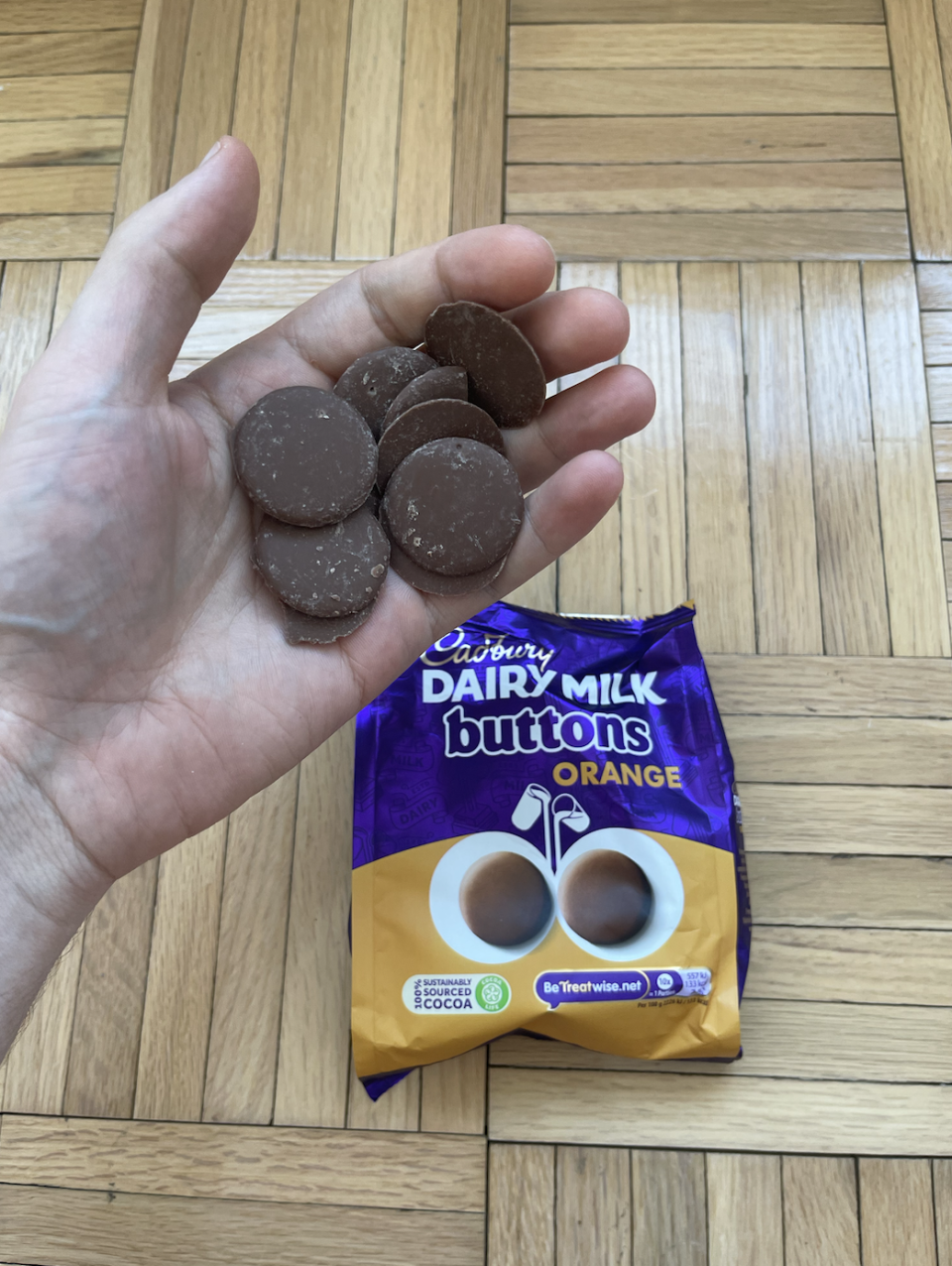 Hand holding several Cadbury Dairy Milk orange chocolate buttons above an opened packet