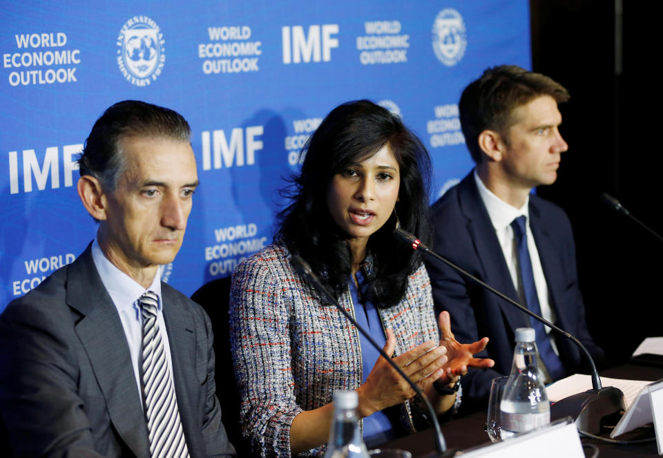 Gita Gopinath speaks at an IMF press conference, flanked by two men.