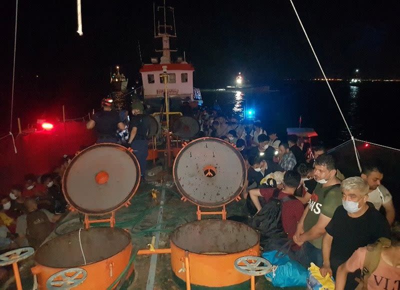 Members of Turkish Coast Guard Command stand guard next to migrants on the deck of a cargo ship during a raid in Izmir