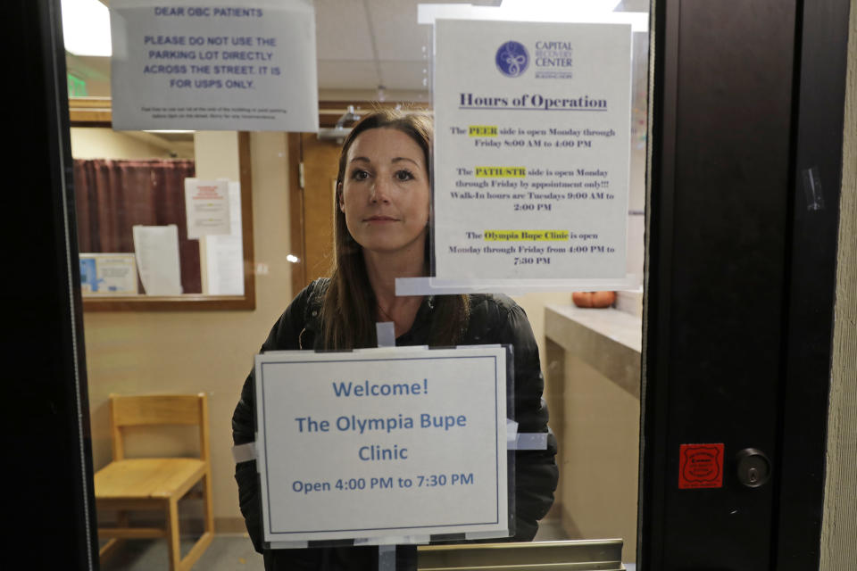 CORRECTS TO CAPITAL, NOT CAPITOL- In this Nov. 14, 2019 photo, Jamie Cline poses for a photo behind a glass window in a door at the Olympia Bupe Clinic at the Capital Recovery Center in Olympia, Wash., which helps people addicted to heroin and other opiates get prescriptions for buprenorphine, a medicine that prevents withdrawal sickness in people trying to stop using opiates. At the clinic, a doctor is working to spread a philosophy called "medication first," which scraps requirements for counseling, abstinence or even a commitment to recovery in the battle against opioid addiction. (AP Photo/Ted S. Warren)