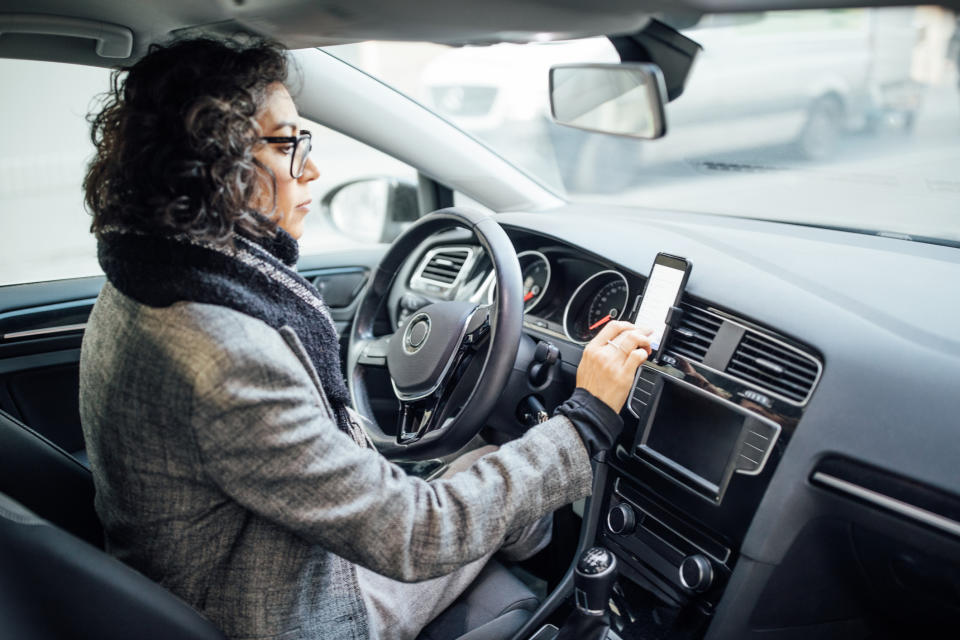 A woman drives while pressing buttons on her phone