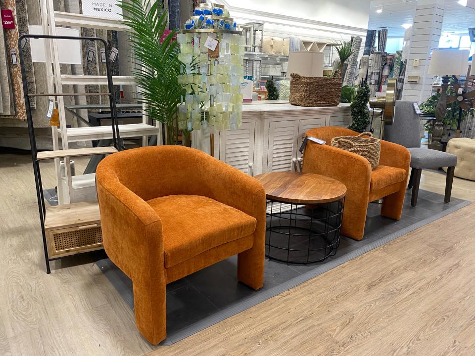 orange armchairs on a gray carpet in a homegoods display with a round wood table between them