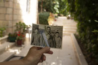 Samira Dajani holds a photo of her father, Fouad Moussa Dajani and his sons, taken in the same place in the courtyard of their home in the Sheikh Jarrah neighborhood of east Jerusalem, Sunday, May 9, 2021. When Samira Dajani's family moved into their first real home in 1956 after years as refugees, her father planted trees in the garden, naming them for each of his six children. (AP Photo/Maya Alleruzzo)