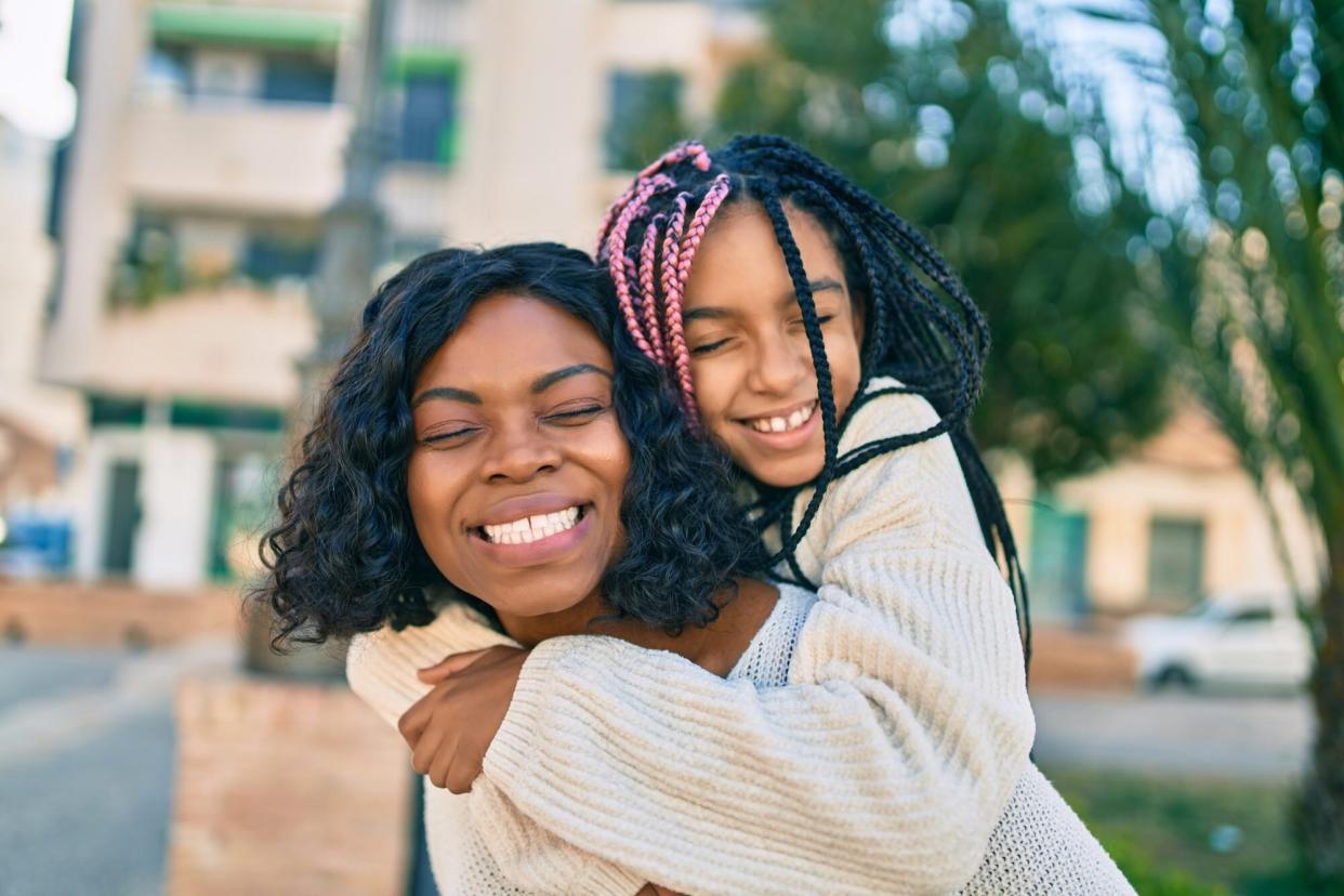 Beautiful african american mother giving daughter piggyback ride smiling happy at the park.