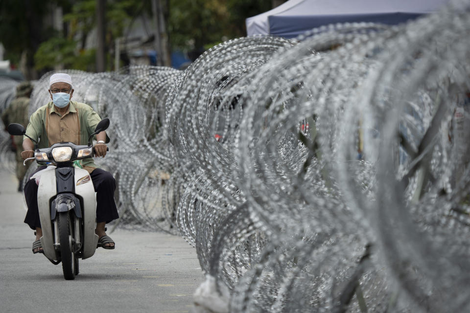 A motorcyclist rides along a barbed wire fence in the virus lockdown area of Selayang Baru, outside Kuala Lumpur, Malaysia, on Sunday, April 26, 2020. The lockdown was implemented to allow authorities to carry out screenings to help curb the spread of coronavirus. (AP Photo/Vincent Thian)