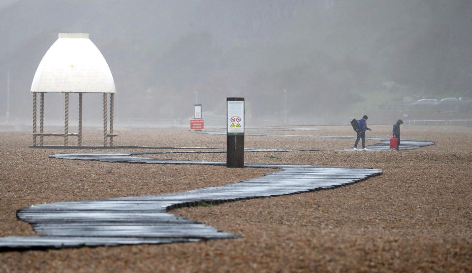 People walk along the beach in Folkestone, as the effects of Storm Dennis continue to cause problems across the country, in Kent, England, Sunday, Feb. 16, 2020. Storm Dennis roared across Britain on Sunday, lashing towns and cities with high winds and dumping so much rain that authorities urged residents to protect themselves from "life-threatening floods" in Wales and Scotland. (Gareth Fuller/PA via AP)