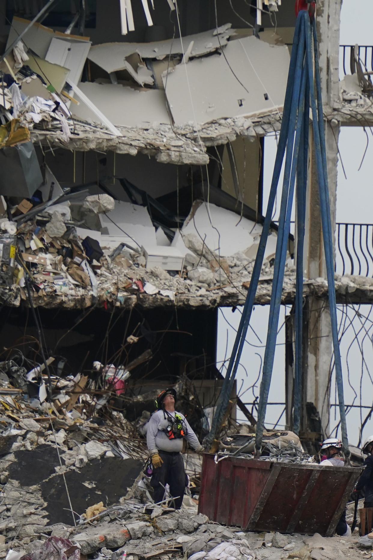 A crane prepares to remove a load of debris and household items as search and rescue personnel work atop the rubble at the Champlain Towers South condo building, where scores of people remain missing almost a week after it partially collapsed, on Wednesday, June 30, 2021, in Surfside, Fla.
