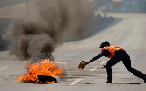 A police officer tries to put out a fire during a demonstration in Caracas - Credit: AFP
