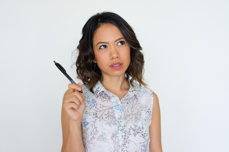 A young woman holds a pen and ponders something.