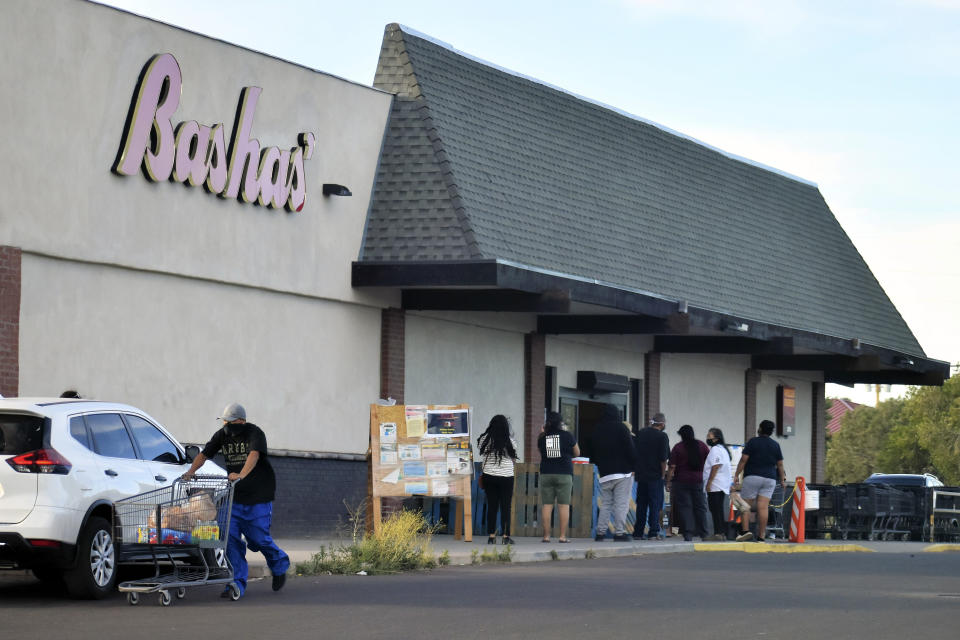 In this Thursday, June 25, 2020 photo provided by C.M. Clay, shoppers wait in line outside a grocery store in Whiteriver, Ariz., on the Fort Apache Indian Reservation. The reservation, home to the White Mountain Apache Tribe, will be under lockdown this weekend to help slow the spread of the coronavirus. (C.M. Clay/White Mountain Apache Tribe via AP)