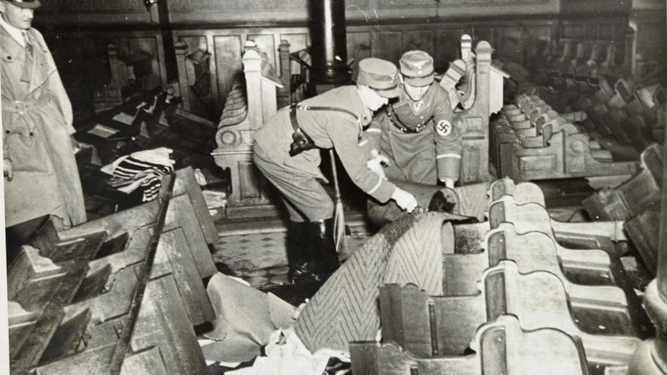 Oficiales nazis vertiendo gasolina en los bancos de una sinagoga