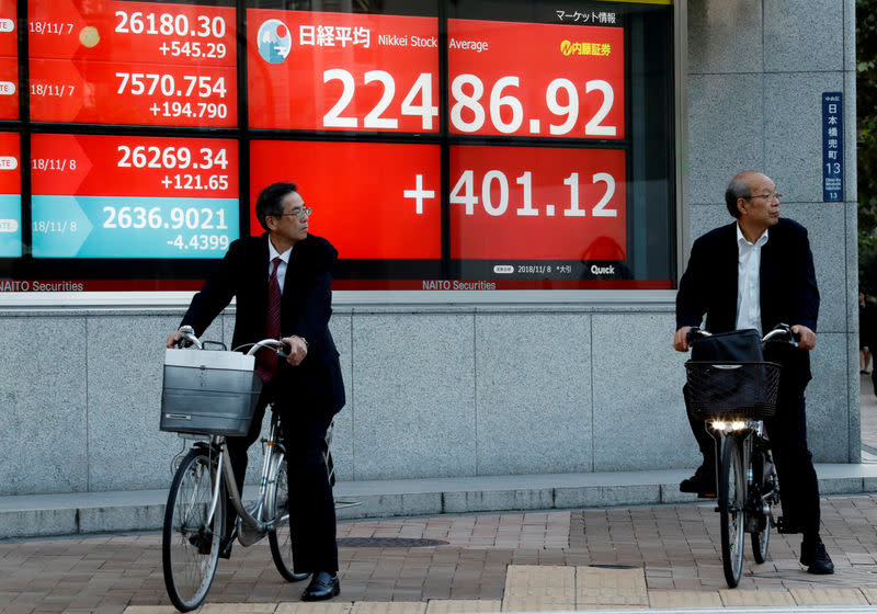 FILE PHOTO: Men riding bicycles stand in front of an electronic board showing Japan's Nikkei average outside a brokerage in Tokyo, Japan, November 8, 2018. REUTERS/Kim Kyung-Hoon/File Photo