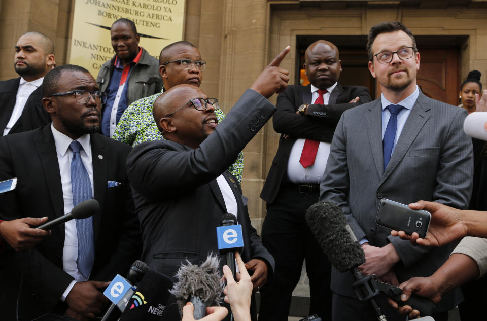 Nelson Mandela Foundation's CEO, Sello Hatang, centre, points to a South African Flag as he speaks to the media on the steps of the Johannesburg High Court, Wednesday, Aug. 21, 2019. South Africa's Equality Court has restricted the display of the old apartheid-era flag in a ruling issued Wednesday Aug. 21, 2019, that it's gratuitous use amounts to hate speech and racial discrimination. (AP Photo/Denis Farrell)