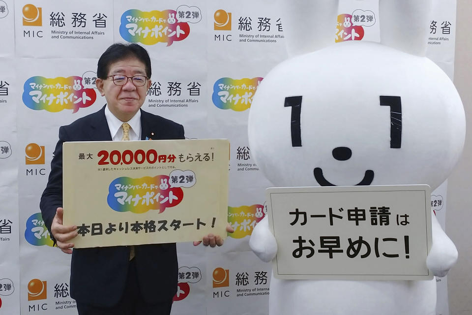 Japan's Minister of Internal Affairs and Communications Yasushi Kaneko attends an event to promote My Number cards in Tokyo on June 30, 2022. Japan has stepped up its push to catch up on digitization by telling a reluctant public they have to sign up for digital IDs or possibly lose access to their public health insurance. The sign, right, reads " Apply for My Number card as soon as possible!" (Kyodo News via AP)