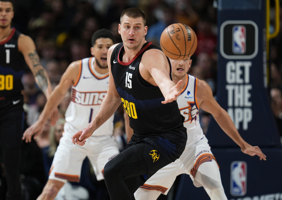 Denver Nuggets center Nikola Jokic, front, juggles the ball as Phoenix Suns guards Grayson Allen, right, and Devin Booker defend during the first half of an NBA basketball game Wednesday, March 27, 2024, in Denver. (AP Photo/David Zalubowski)