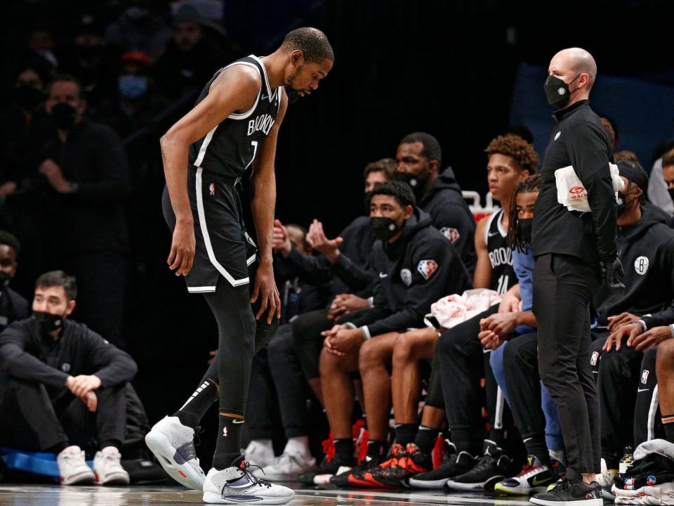 Kevin Durant walks over to the Nets bench while holding his knee during a game.