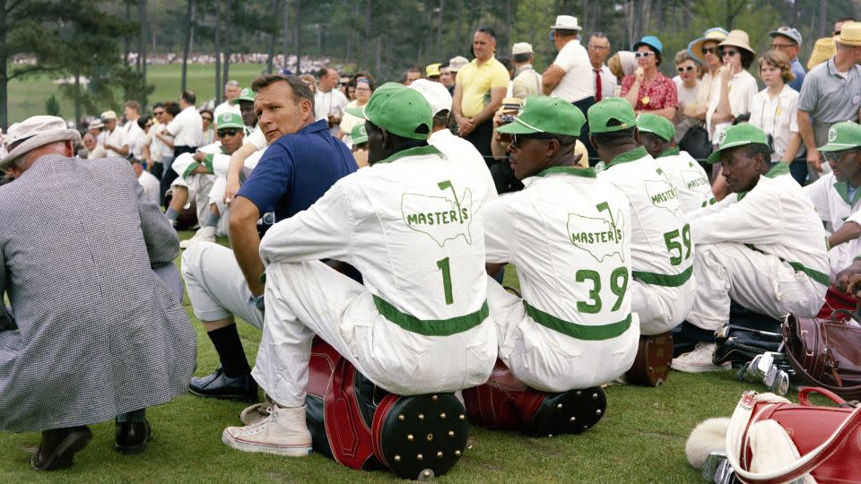 Palmer looks over his shoulder as he sits with a group of caddies during the 1965 Masters. - Augusta National/Getty Images