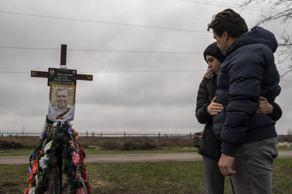 Yura Nechyporenko, 15, hugs his uncle Andriy Nechyporenko above the grave of his father Ruslan Nechyporenko at the cemetery in Bucha, on the outskirts of Kyiv, Ukraine, on Thursday, April 21, 2022. The teen survived an execution attempt by Russian soldiers while his father was killed, and now his family seeks justice. (AP Photo/Petros Giannakouris)