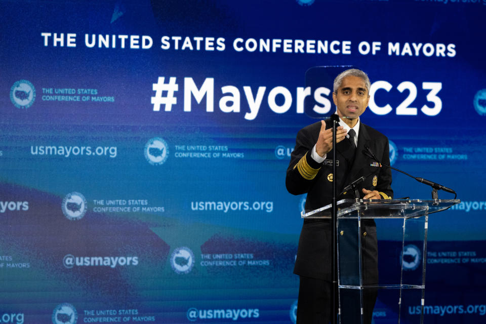 Surgeon General Vivek Murthy at a podium with a a backdrop saying: The United States Conference of Mayors, #Mayors C23. 