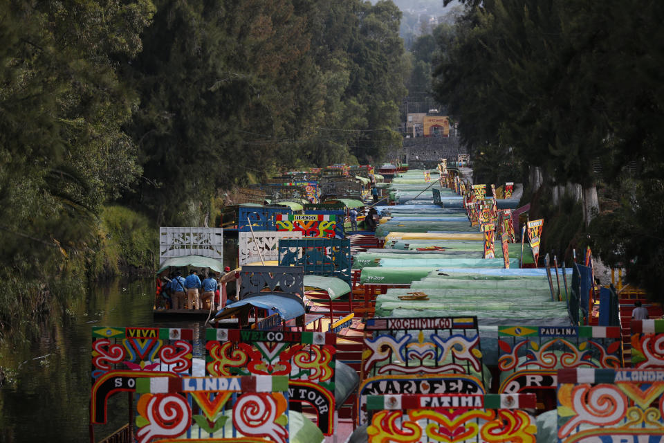 A boat carrying passengers and a band playing live music pass beside dozens of parked trajineras, the colorful boats typically rented by tourists, families, and groups of young people, in Xochimilco, Mexico City, Friday, Sept. 6, 2019. The usually festive Nativitas pier was subdued and largely empty Friday afternoon, with some boat operators and vendors estimating that business was down by 80% on the first weekend following the drowning death of a youth that was captured on cellphone video and seen widely in Mexico. Borough officials stood on the pier to inform visitors of new regulations that went into effect Friday limiting the consumption of alcohol, prohibiting the use of speakers and instructing visitors to remain seated.(AP Photo/Rebecca Blackwell)
