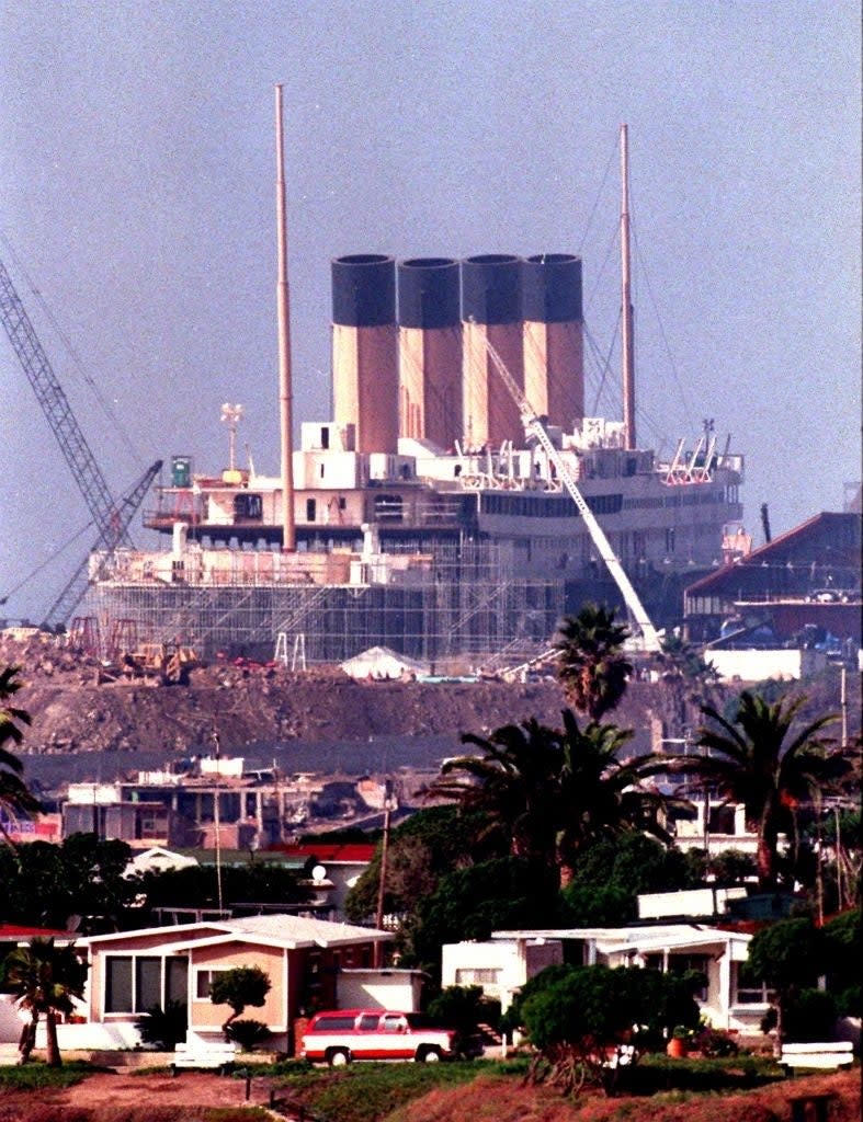 View of a construction site with a ship resembling the famous Titanic being built. Crane and scaffolding are visible. Text on the right reads 