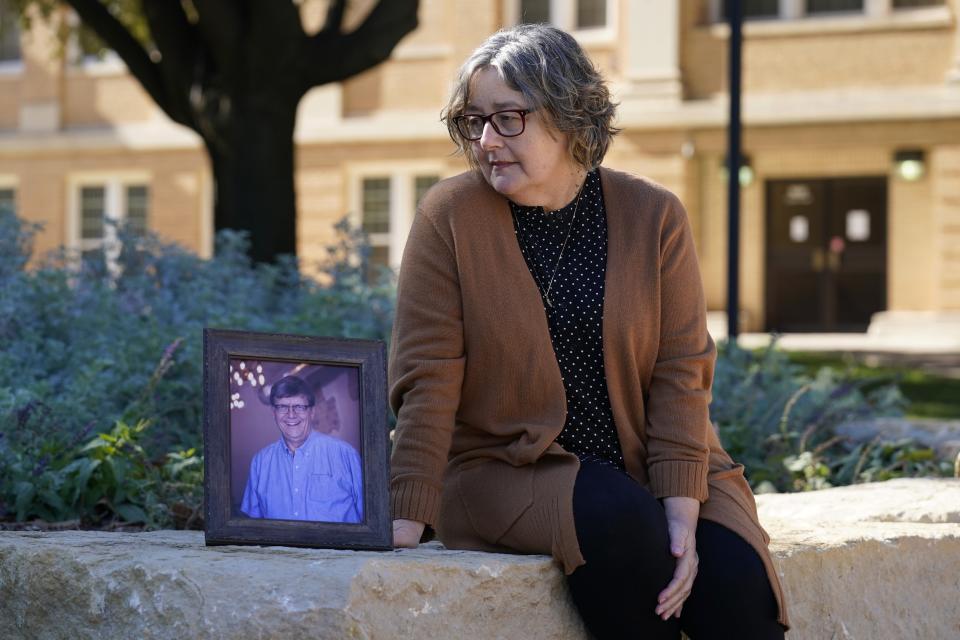 Debbie Riggs poses for a photo, sitting by a portrait of her late husband, Mark Riggs on the campus of Abilene Christian University, Wednesday, Dec. 16, 2020, in Abilene, Texas. Mark, who was a professor at the school, passed away of COVID-19 last Monday. Pressure is intensifying on governors who haven’t issued mandates as new coronavirus cases and deaths soar before Christmas. But the debate over mandates and lockdowns often drowns out the reality of whether the restrictions enacted are actually enforced. In the rugged West Texas town of Abilene, the number of deaths has doubled over the past month and intensive care unit beds have been full for weeks. (AP Photo/Tony Gutierrez)