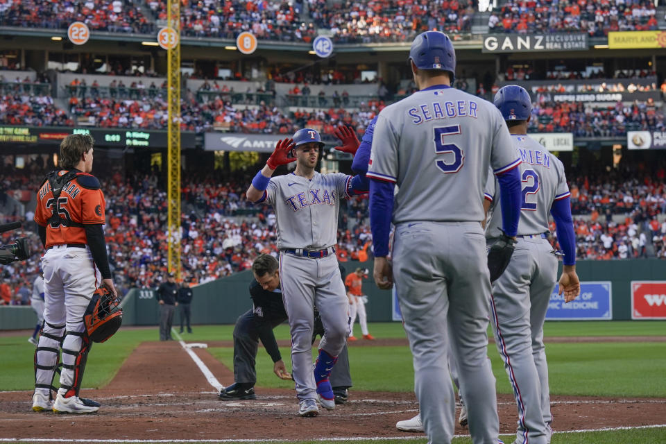 Adley Rutschman, izquierda, receptor de los Orioles de Baltimore, observa como Mitch Garver, centro, de los Rangers de Texas, celebra mientras cruza el plato después de batear un durante la tercera entrada del Juego 2 de la Serie Divisional de la Liga Americana, el domingo 8 de octubre de 2023, en Baltimore. (AP Foto/Julio Cortez)