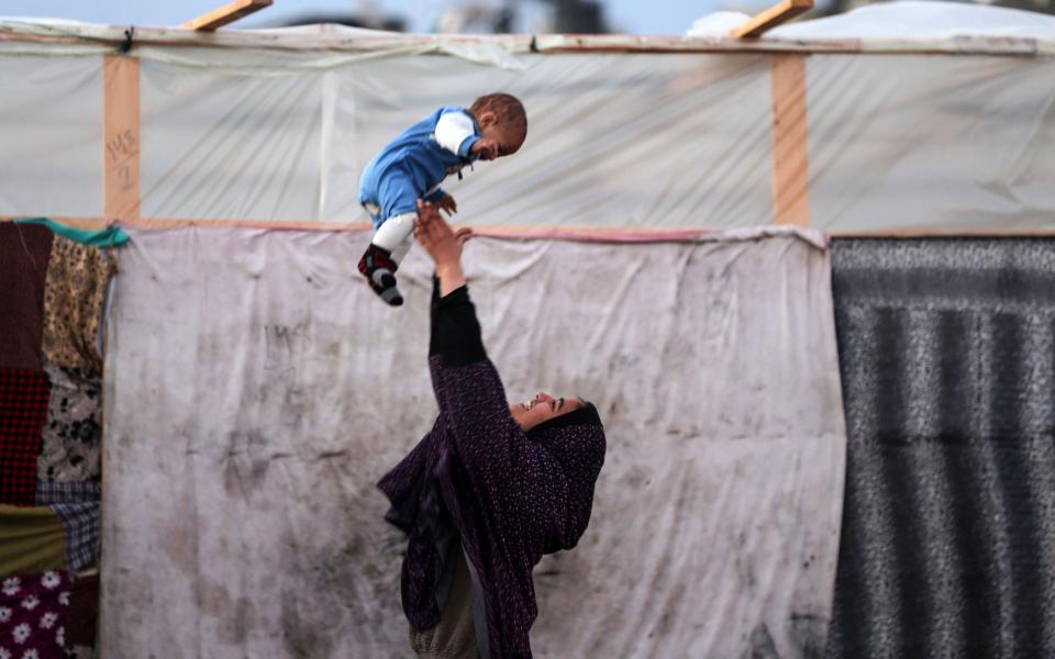 Palestinians are gathering outside makeshift shelters at a camp for displaced Palestinians in Deir al-Balah in the central Gaza Strip