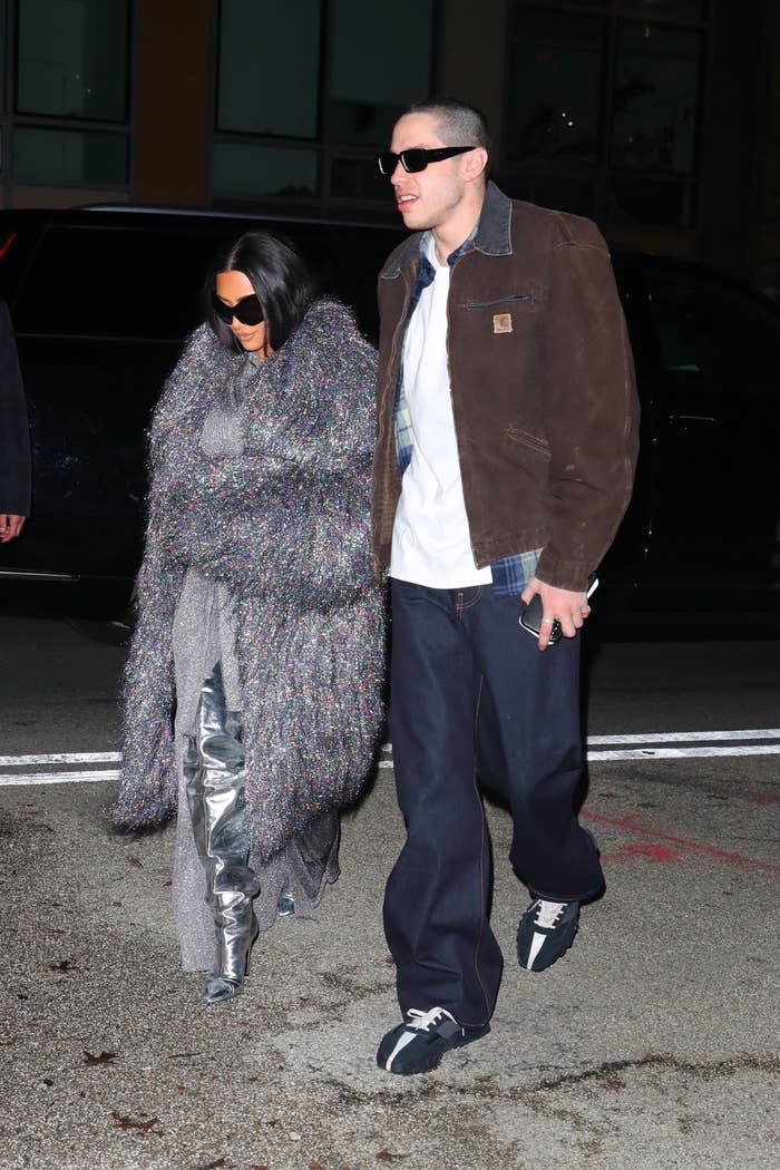 Pete, who's wearing the most basic jeans and jacket possible, wraps his arm around Kim, who's wearing a floor-length holographic confetti coat